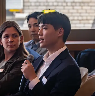 Participant speaking into a microphone during a business event while others listen in the audience