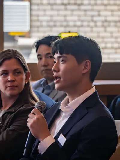Participant speaking into a microphone during a business event while others listen in the audience