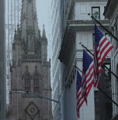 Historic building framed by tall city structures with U.S. flags lining the street in the foreground