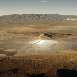 An aerial view of multiple Hanwha solar PV panels installed throughout a vast valley with a mountain range across the background