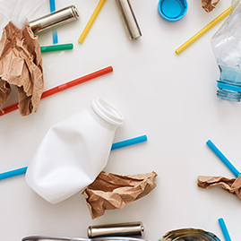 A crumpled, white plastic bottle, a blue straw, and pieces of discarded brown craft paper lay scattered across a white background