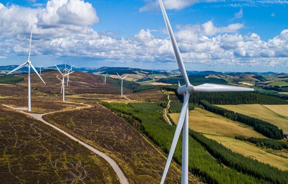Massive wind turbines surrounded by rolling hills generate clean energy beneath a bright blue sky