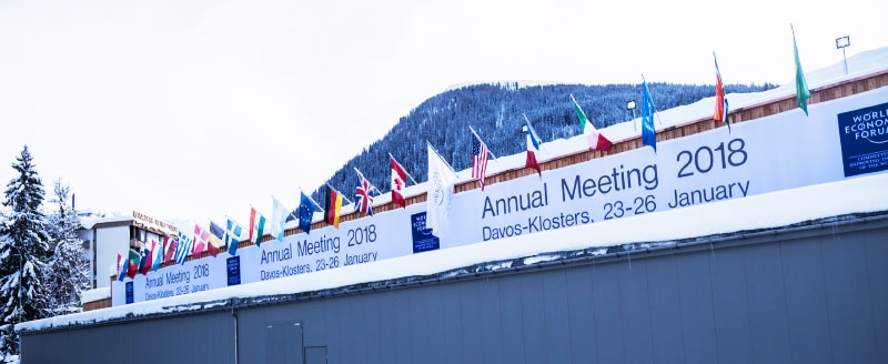Flags hang above a sign for the WEF's 2018 Annual Meeting in Davos, Switzerland, recognized for its renewable energy measures.