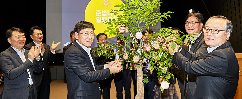 韩华Aerospace代表申铉宇（左三）、韩华精密机械和韩华Techwin代表金渊喆（右）将写有激励寄语的便条挂在“合规”树木上