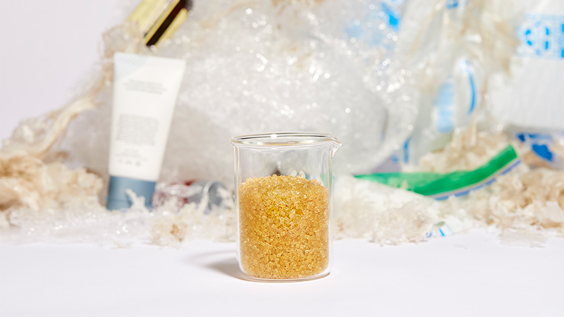 A vial filled with Novoloop’s Oistre™ technology in front of a pile of plastic waste. 