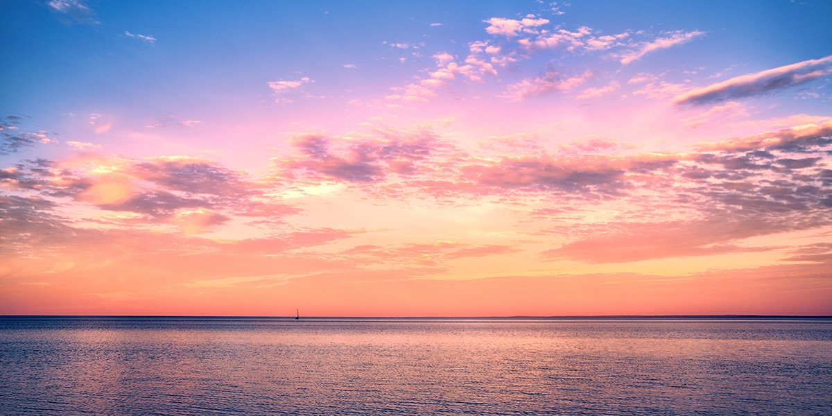 A sunset over an ocean, with multiple hues of colors spreading across the sky.