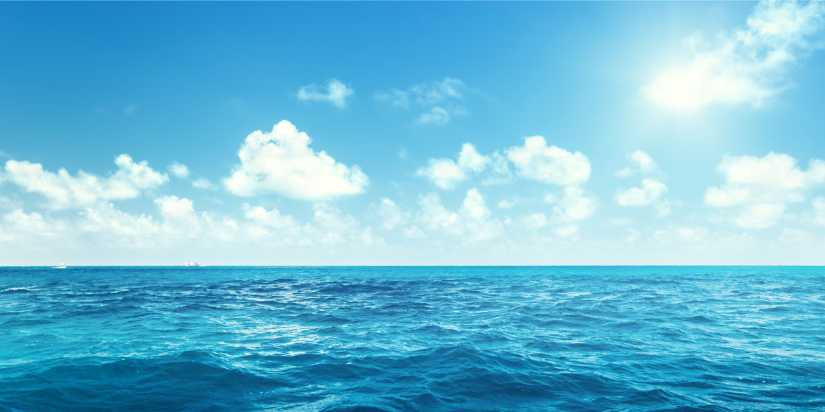 The horizon of a blue ocean meets a sunny sky dotted with clouds.