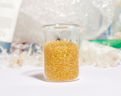 A vial filled with Novoloop’s Oistre™ technology in front of a pile of plastic waste. 