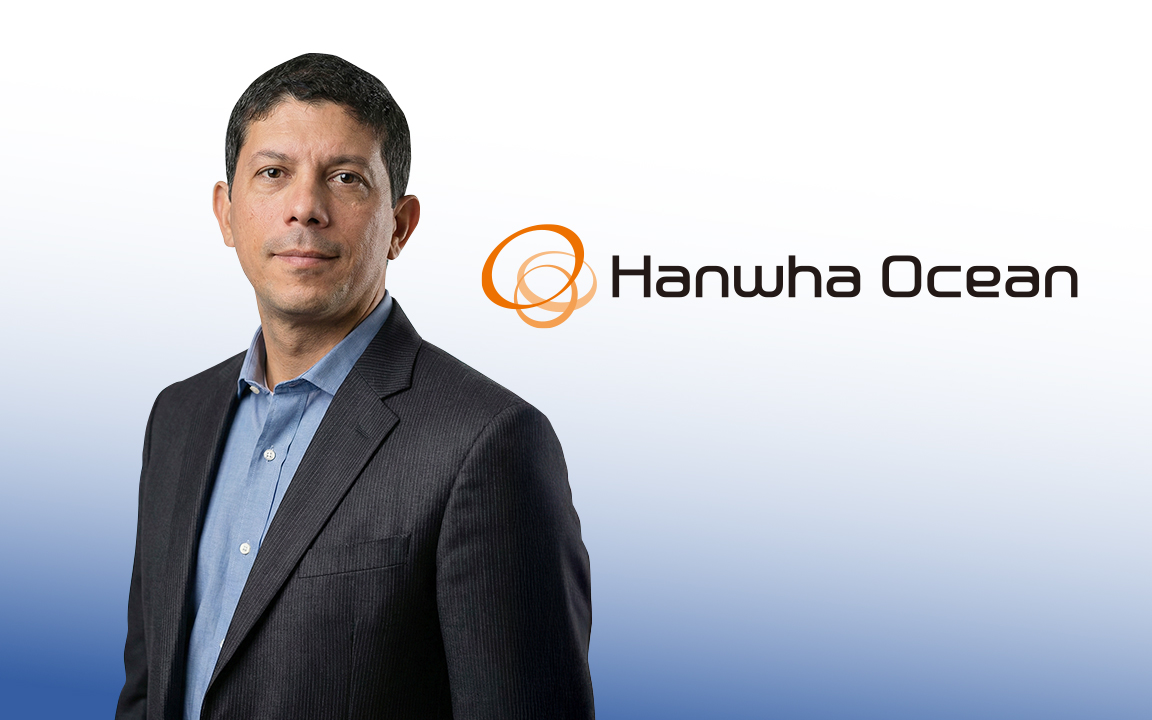 Weverton Nazario, Head of Operations and Maintenance at Hanwha Ocean, in a dark suit, standing against a gray wall  