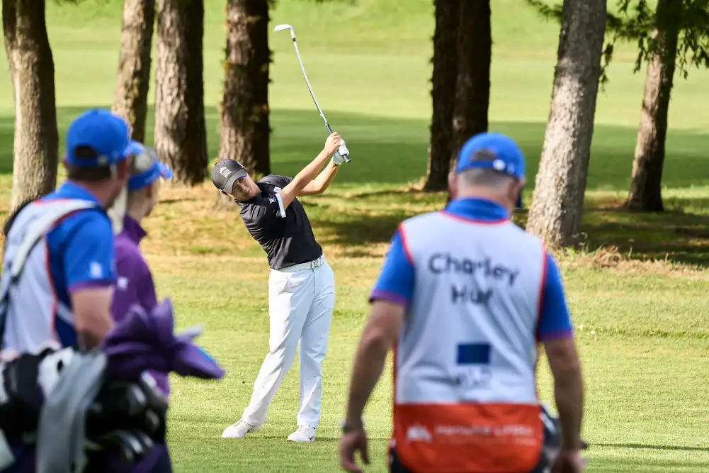 A Korean golfer hits an iron shot from the fairway as opponents and caddies watch.