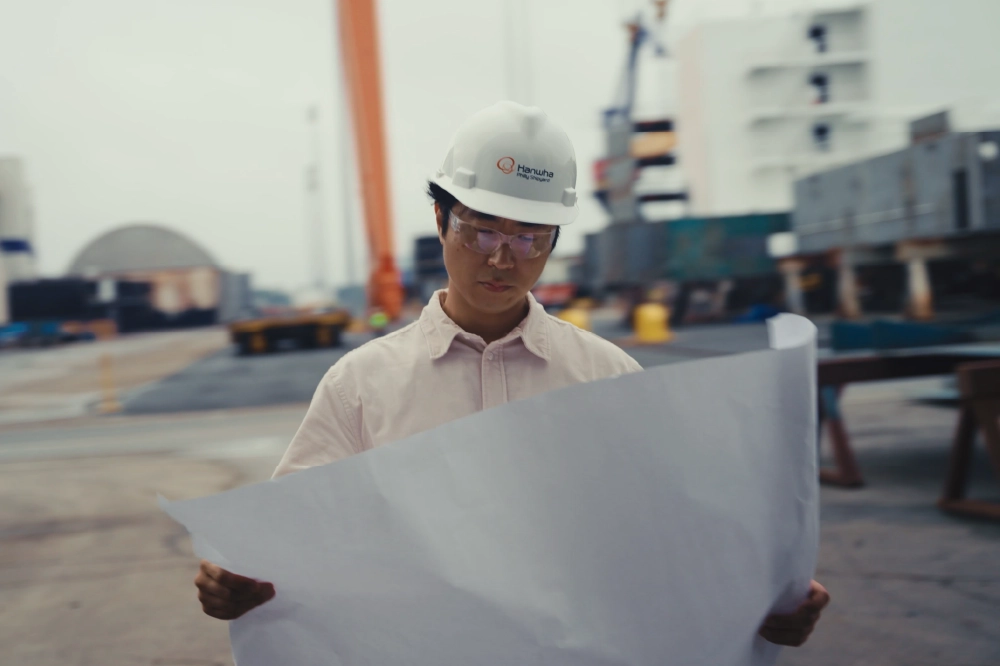 A dual graphic with a man wearing a hard hat looking at plans at Hanwha Philly Shipyard and a man welding on an orange rig.