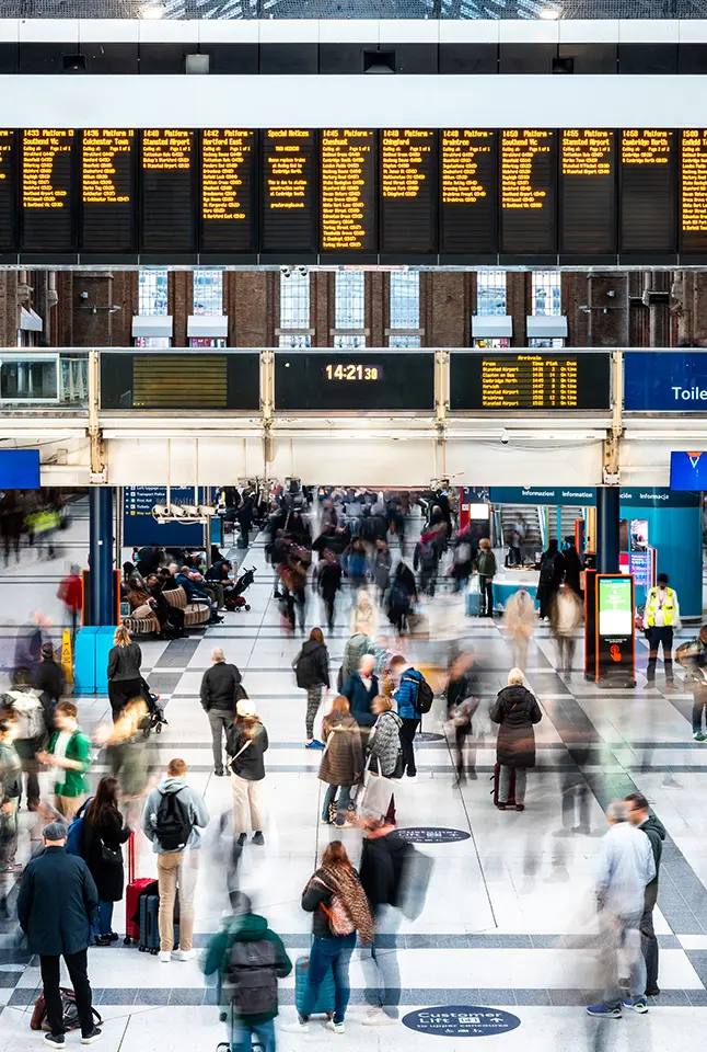 A busy crowd walks around in a train station concourse.