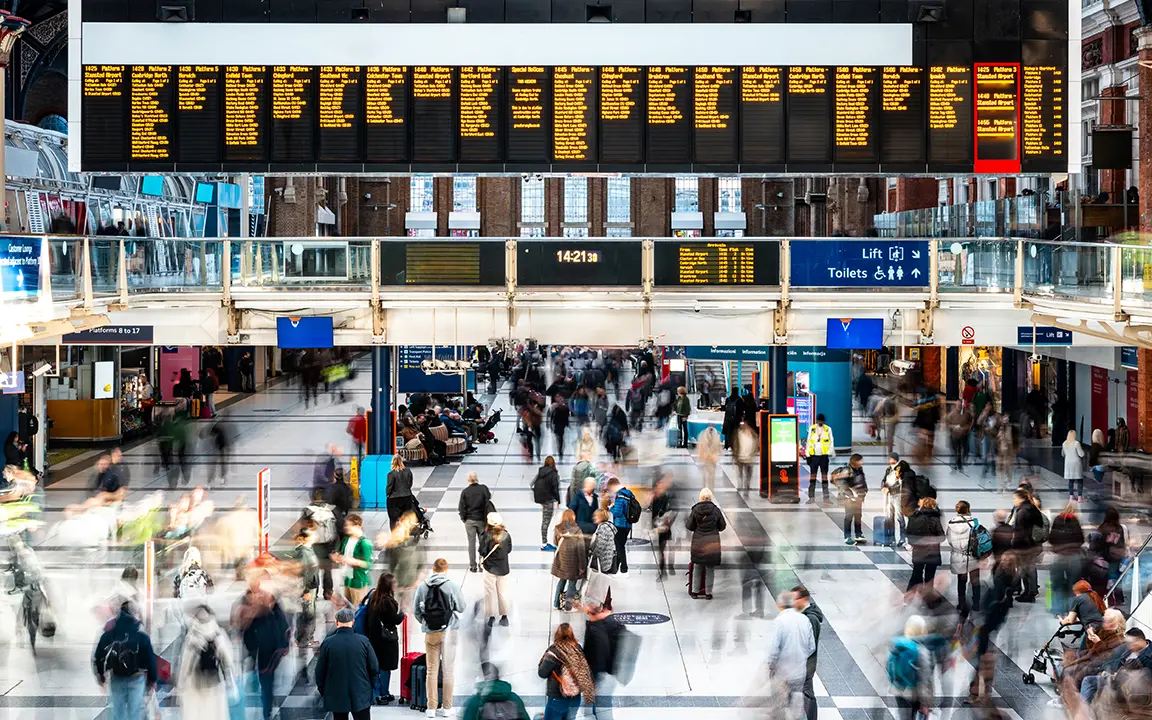 A busy crowd walks around in a train station concourse