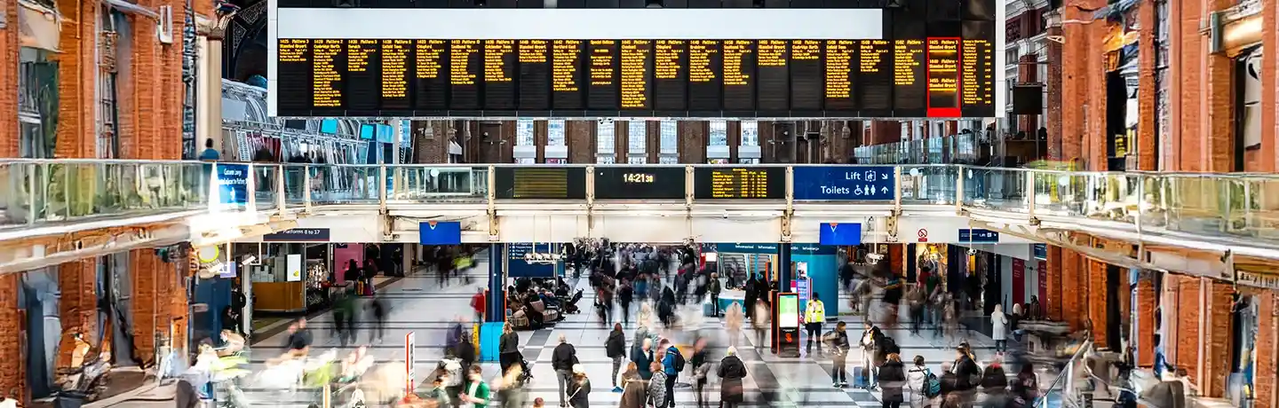 A busy crowd walks around in a train station concourse